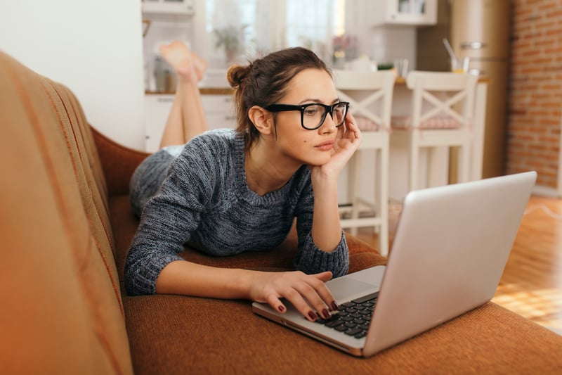 wanita muda dalam posisi santai mengerjakan laptopnya di rumah